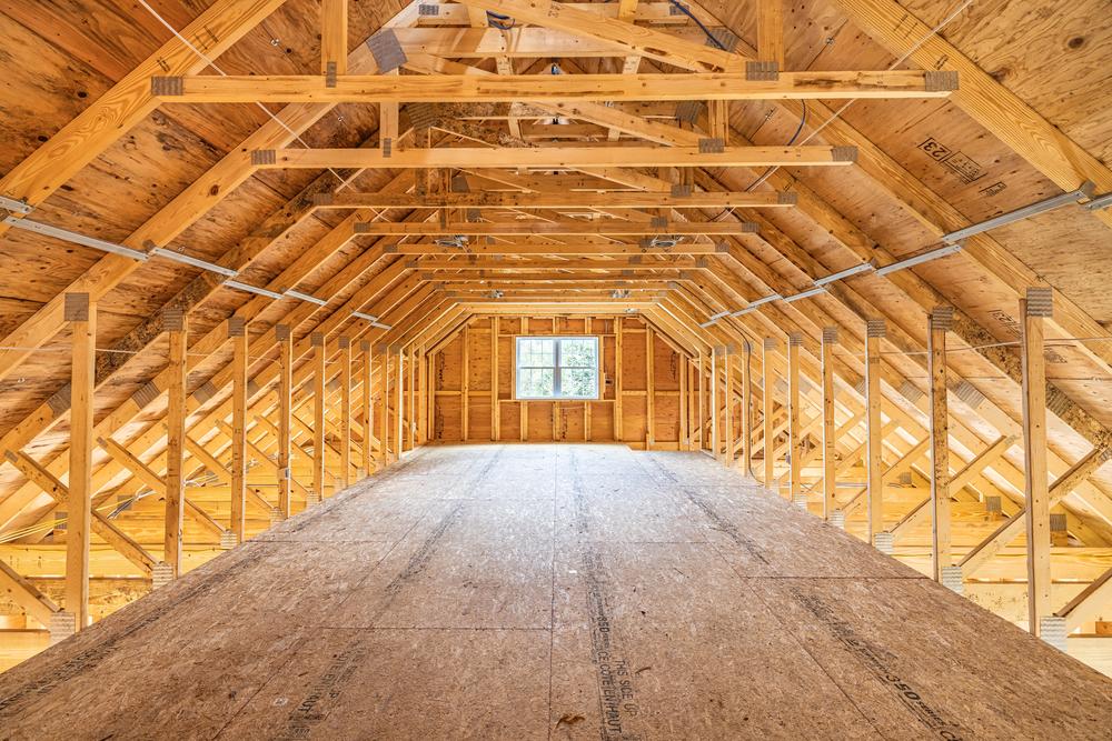 Commercial construction interior showing a framed loft area with engineered roof trusses, plywood flooring, and exposed structural supports during building construction.