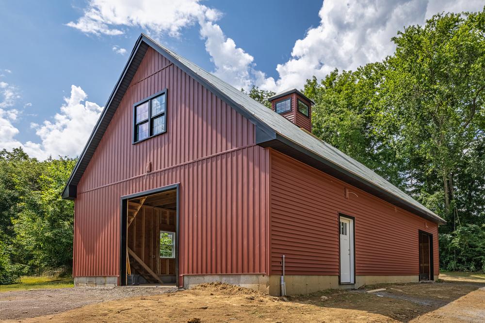 Commercial construction of a newly built post-frame building with red metal siding, open bay door, and finished roof structure on a cleared site.