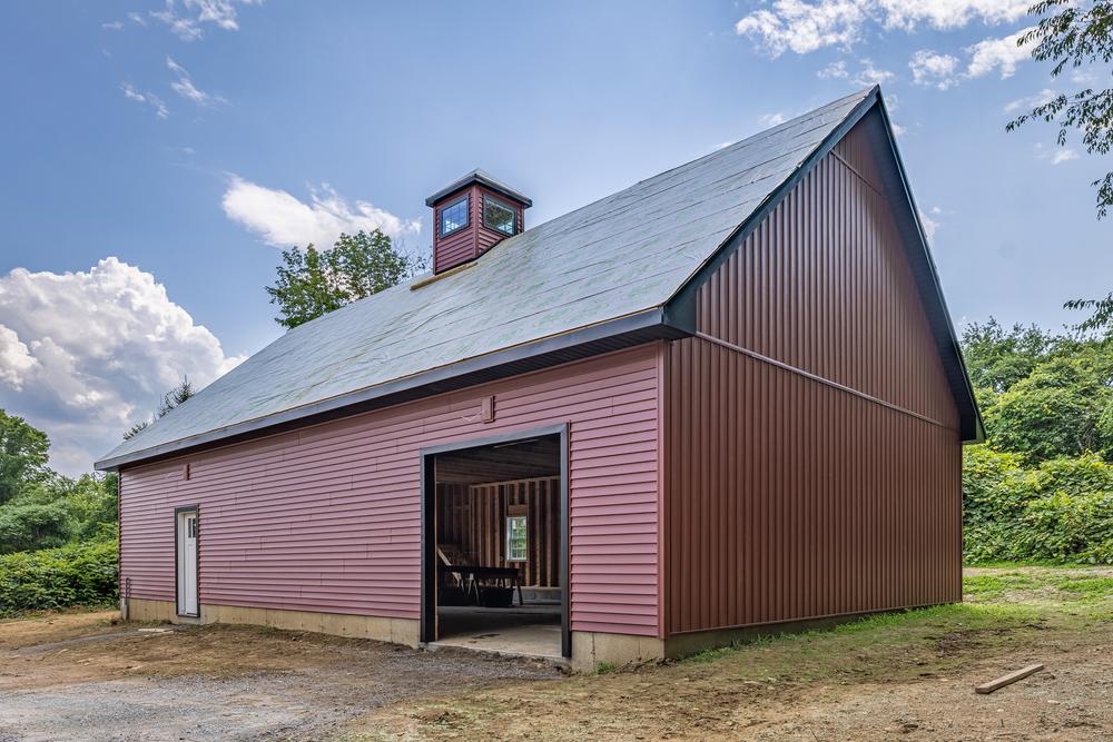 Commercial construction project featuring a post-frame building with finished metal siding, completed roof, and open bay entrance nearing final completion.