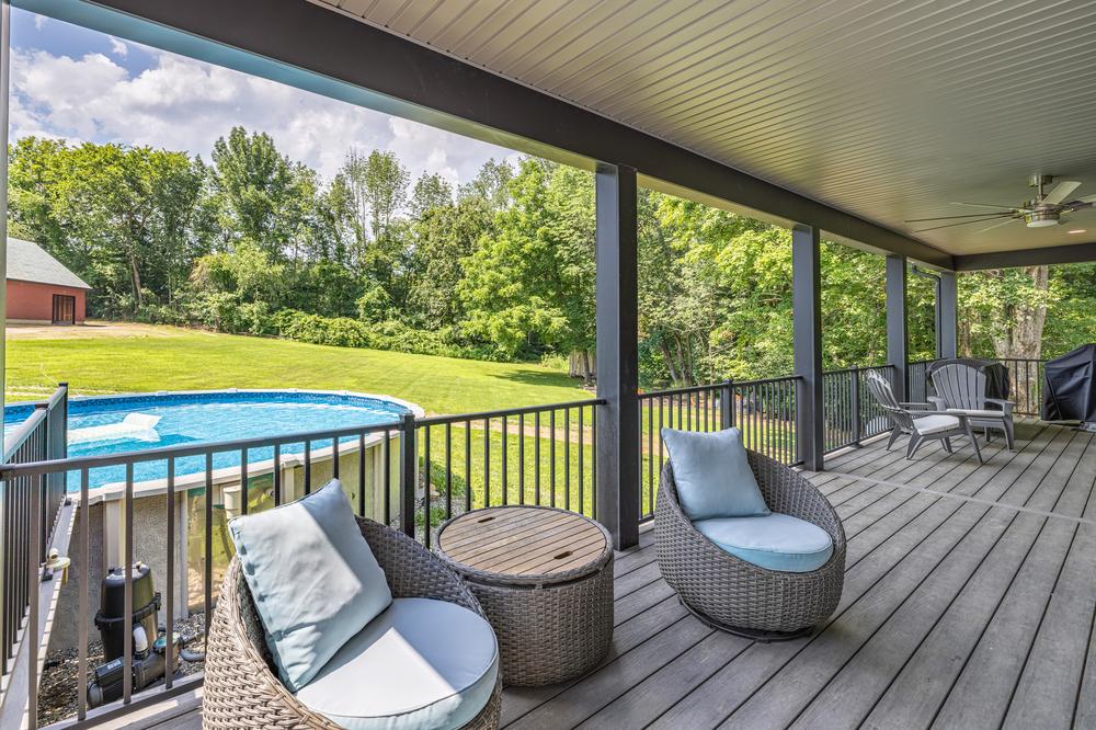 Residential construction exterior featuring a covered deck with modern railing, seating area, and views of a landscaped yard and pool, designed for outdoor living and entertaining.