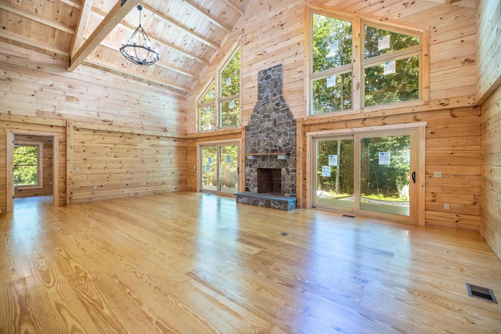 Residential construction interior showcasing a custom living room with vaulted wood ceilings, exposed beams, natural hardwood floors, large windows, and a stone fireplace as part of a high-end home build.