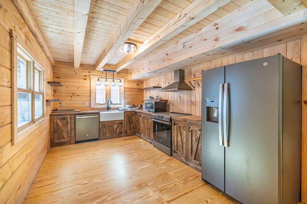 Residential construction kitchen renovation featuring a rustic log-style design with custom wood cabinetry, farmhouse sink, stainless steel appliances, exposed beam ceiling, and natural wood flooring.