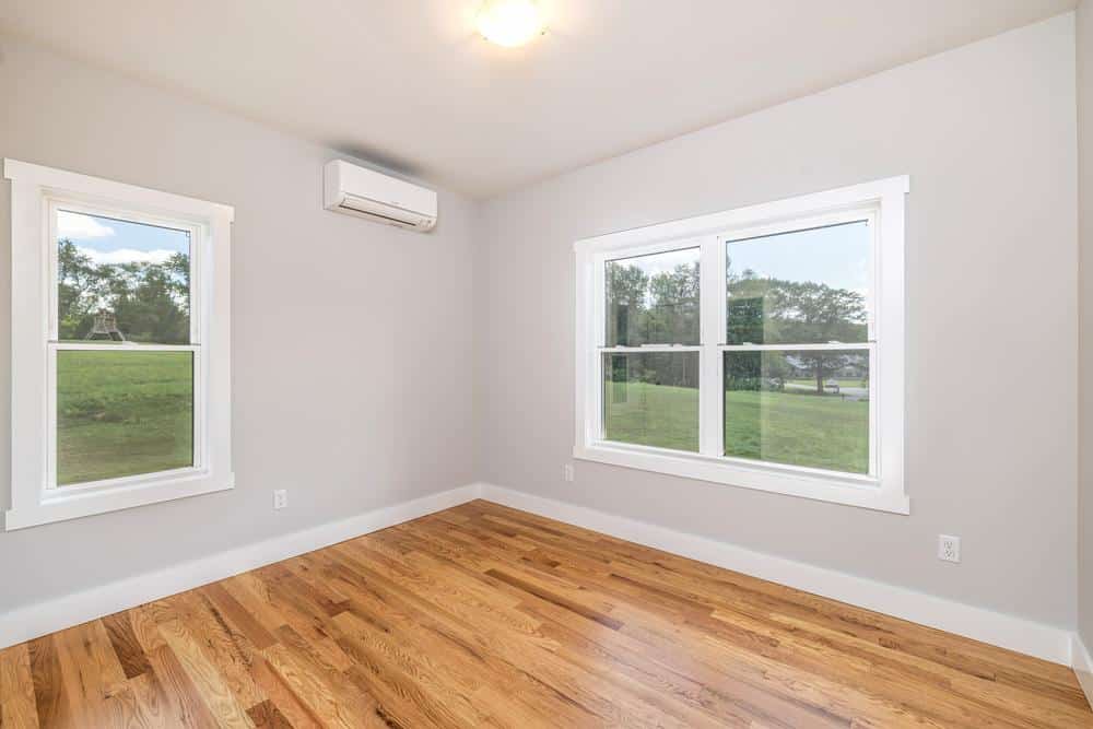 Bright finished bedroom with hardwood floors, large windows, and neutral walls, showcasing quality residential construction and clean interior craftsmanship.
