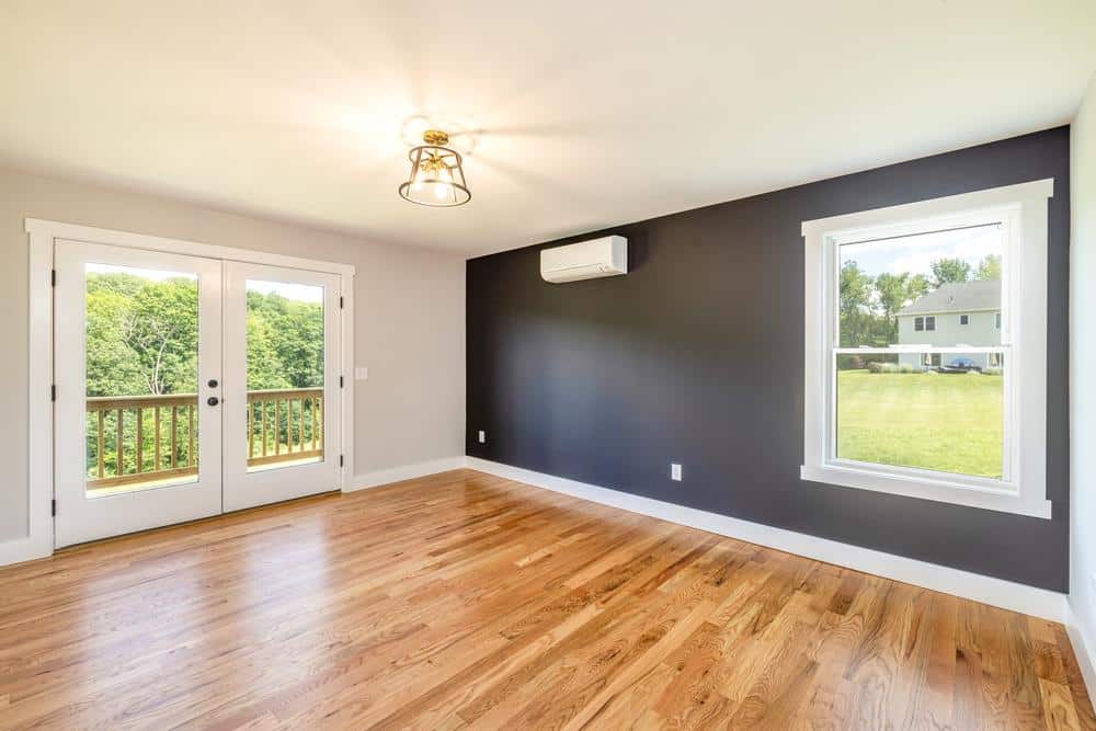 Bright finished living room with hardwood floors, dark accent wall, mini-split system, large windows, and French doors to a deck, completed as part of residential construction and excavation services supporting the home build.