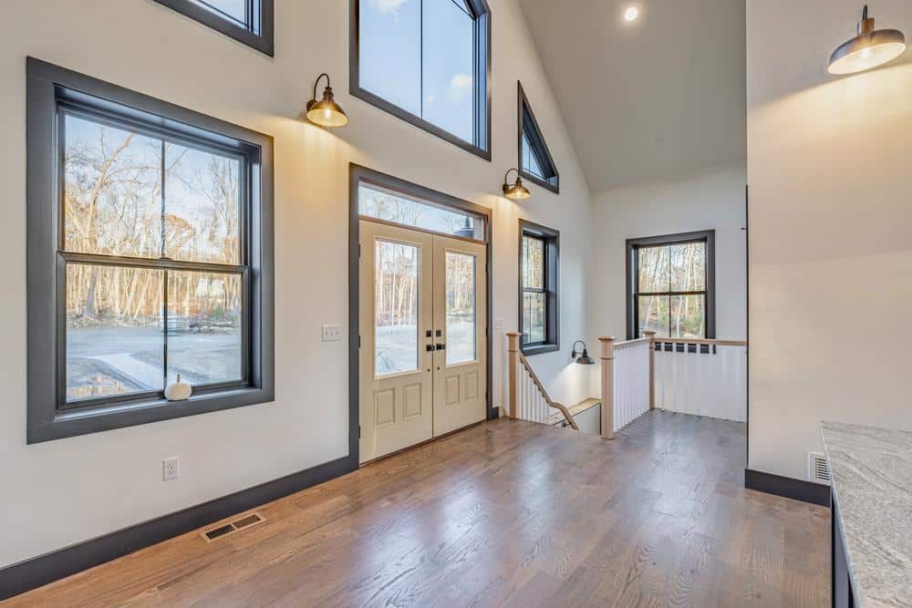 Residential construction interior highlighting an open living space connected to a kitchen renovation, with hardwood flooring, large windows, vaulted ceilings, and custom trim throughout.