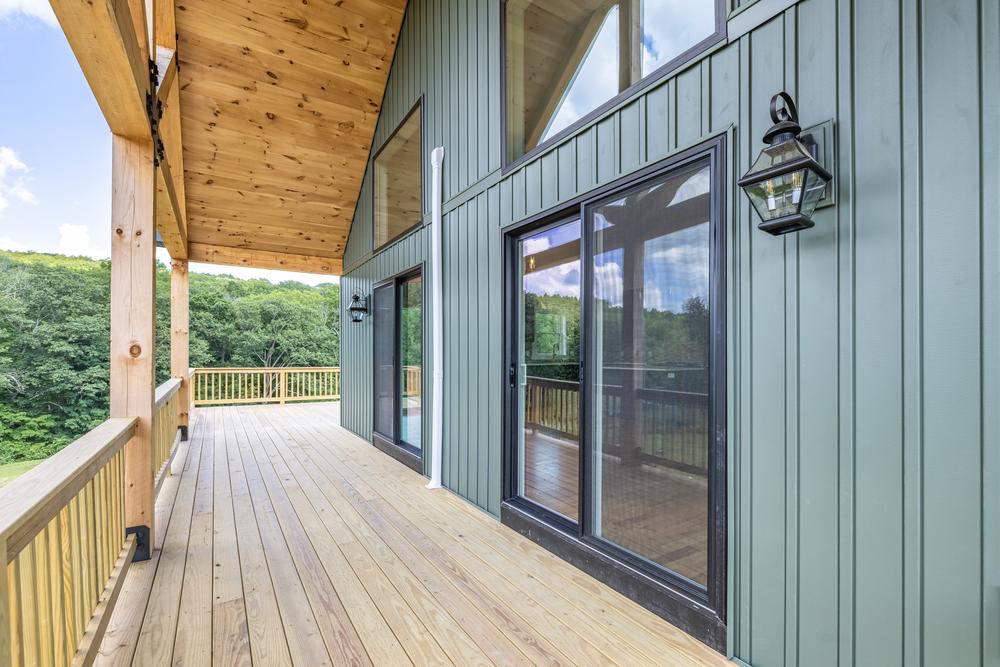 Residential construction exterior showing a covered wooden deck with sliding glass doors and green vertical siding, highlighting custom home construction, outdoor living space, and quality craftsmanship.