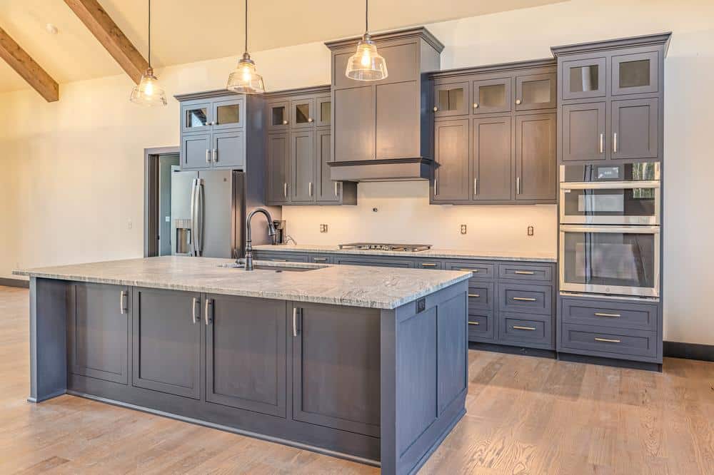 Residential construction kitchen renovation featuring custom cabinetry, a large center island with stone countertop, pendant lighting, and built-in stainless steel appliances.