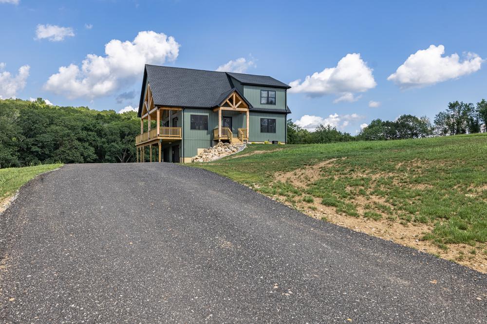 Residential construction exterior showing a newly built custom home with a covered porch, hillside lot, and freshly paved driveway, highlighting a completed home build on a rural jobsite.