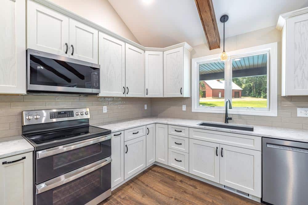 Residential construction kitchen renovation featuring white shaker cabinetry, stainless steel appliances, stone countertops, subway tile backsplash, and a window overlooking the property.