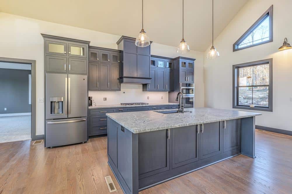 Residential construction kitchen renovation showcasing a modern open layout with custom cabinetry, a large stone island, stainless steel appliances, and natural light from oversized windows.