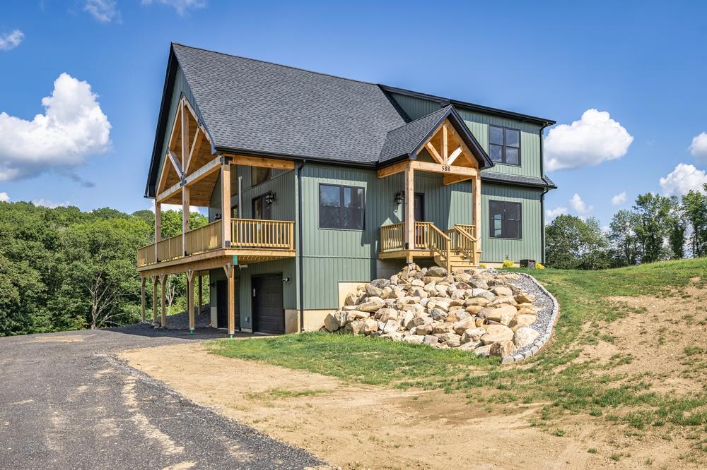 Residential construction exterior highlighting a custom-built home with a wraparound porch, timber framing, stone retaining wall, and hillside lot, showcasing professional residential construction craftsmanship.