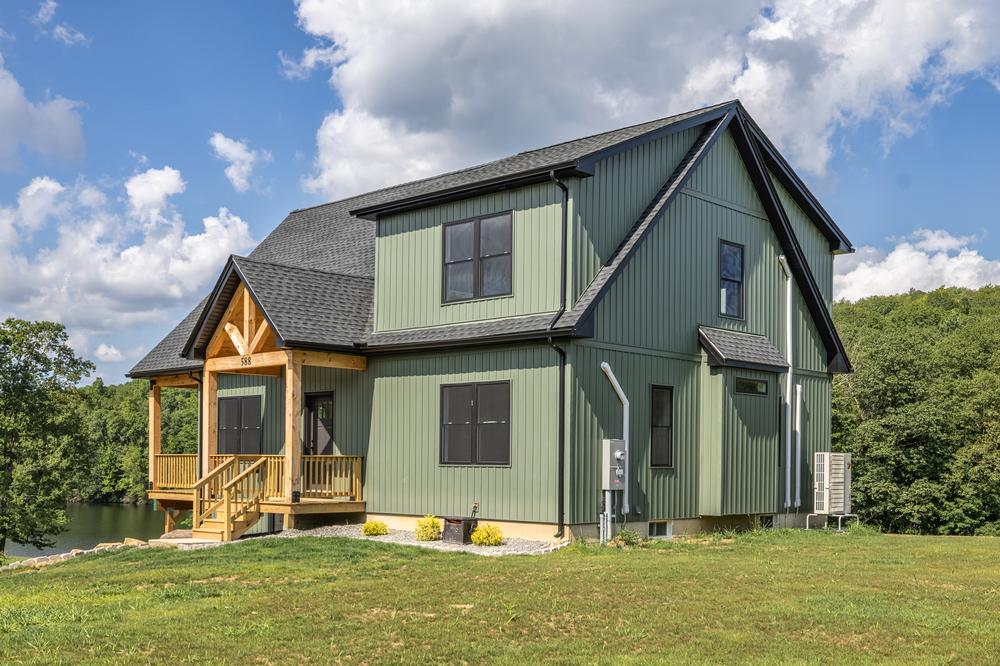 Residential construction exterior featuring a newly completed single-family home with green siding, a covered front porch, and custom wood trim, showcasing a quality home build in a natural setting.