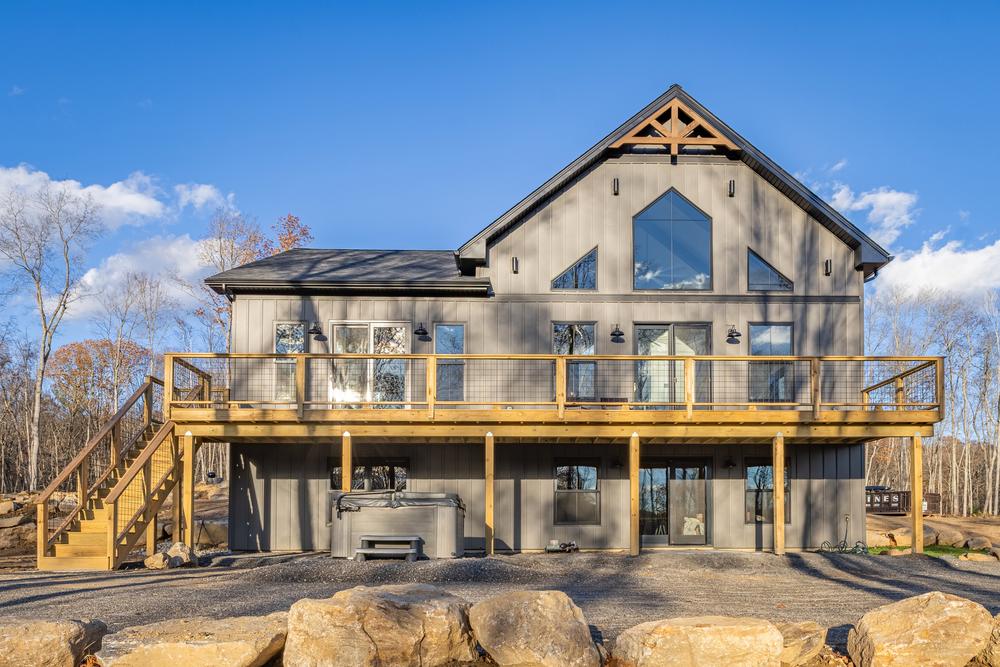 Residential construction exterior featuring a newly built modern home with vertical siding, large windows, and an elevated deck spanning the rear of the house, completed as part of a custom home build.