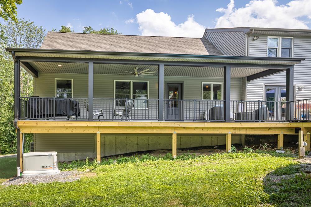 Residential construction exterior showcasing a covered deck addition with modern railing, ceiling fan, and seating area built onto a finished home for expanded outdoor living space.