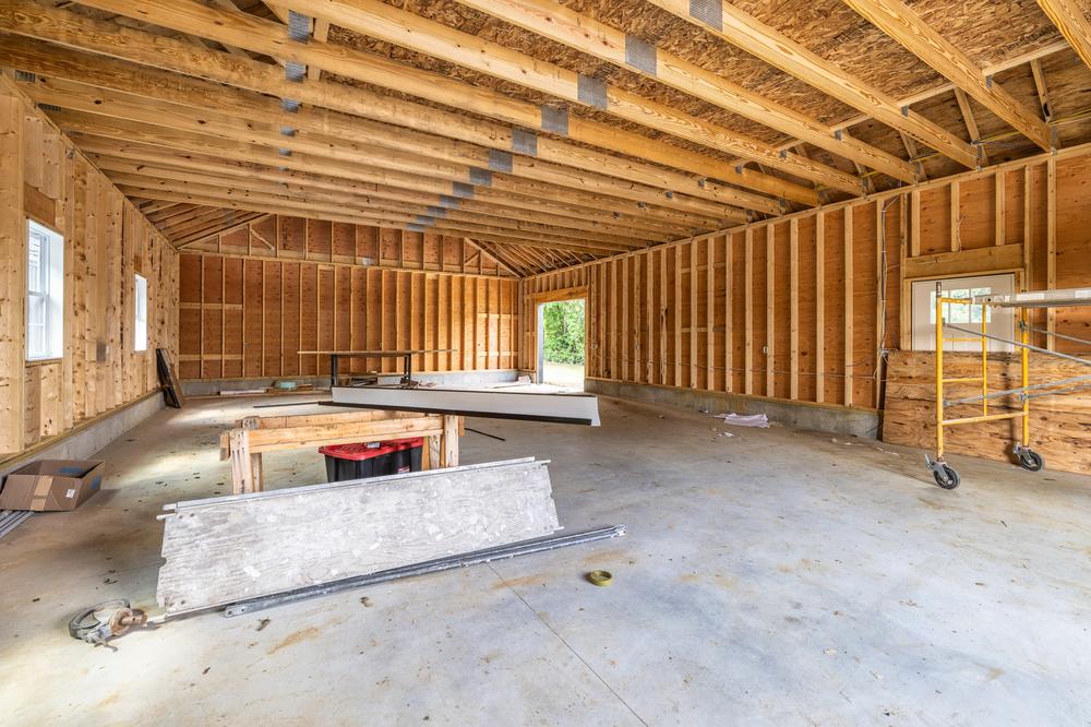Commercial construction interior showing an open post-frame workspace with exposed wood framing, roof trusses, and concrete slab during active build-out work.